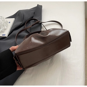 Detail of dark brown glossy leather crossbody bag with pleated cloud design and silver buckle