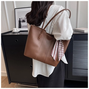 Brown leather tote bag shown on shoulder with silk scarf detail for a chic commuter look