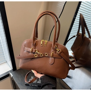Detail of dark brown leather handbag with gold metal rings on a wooden table