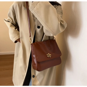 Detail of vintage brown leather bag featuring a golden flower-shaped clasp and slim strap