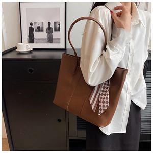 Detailed texture of brown leather tote bag featuring a decorative striped silk scarf