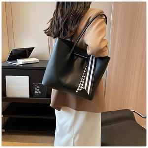 Close-up of black leather tote bag featuring a striped silk scarf and minimalist texture