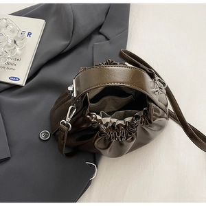 Detail of a retro dark brown pleated cloud bag with shiny leather texture on a grey blazer
