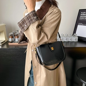 Vintage black saddle bag with glossy leather and gold buckle closure on a trench coat