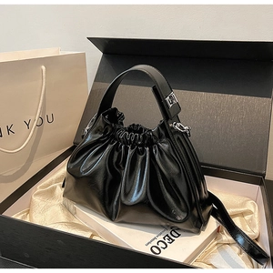 Detailed view of glossy black pleated cloud bag inside a luxury gift box packaging