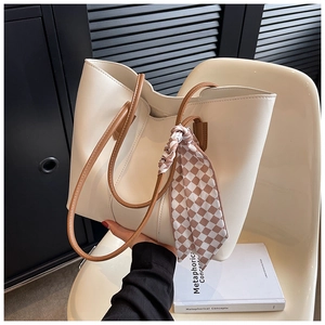 Detail of a creamy white tote bag with brown leather handles and a checkered silk scarf