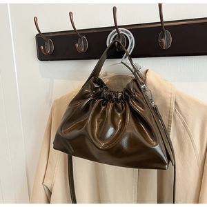 Detail of a brown glossy cloud bag hanging on a wooden hook next to a beige trench coat