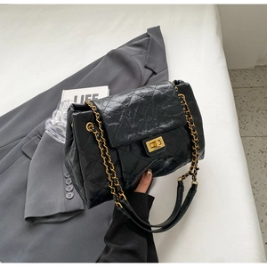 Close-up of black quilted leather bag with gold chain strap and square metal lock