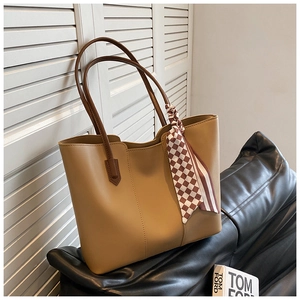 Detail of high-capacity khaki leather tote bag with silk scarf on a black leather seat