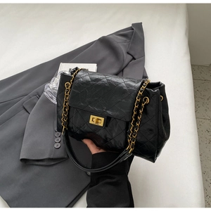 Detail of black quilted oil-wax leather shoulder bag with gold metal clasp and chain
