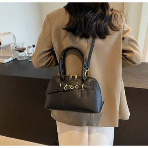 Model wearing a black textured leather shell bag with gold hardware in a cafe setting