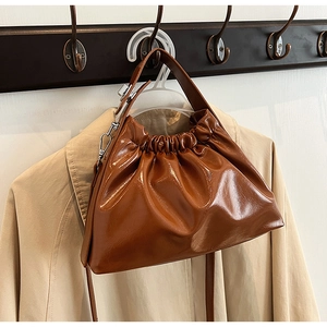 Detail of a brown glossy pleated cloud bag showing smooth leather texture and silver hardware