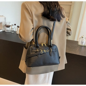 Detail of black pebbled leather handbag with gold hardware and decorative belt strap