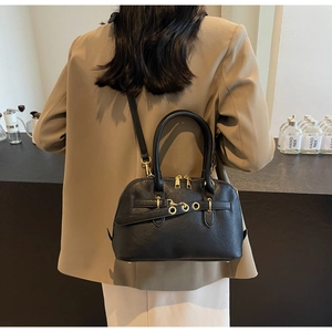 Detail of minimalist black leather boston bag worn with a chic camel blazer for daily look