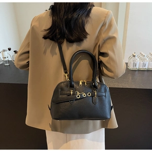 Detail of black pebbled leather shell bag with gold hardware and strap worn by a model