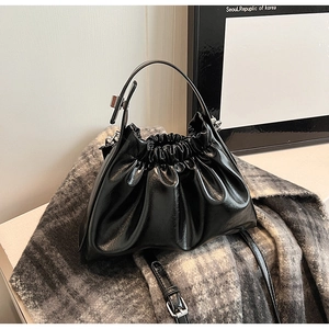 Detail of black patent leather dumpling bag with pleats and metal buckle on scarf
