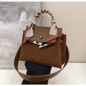 Close-up of brown suede Kelly bag with silk scarf handle and silver metal turn-lock