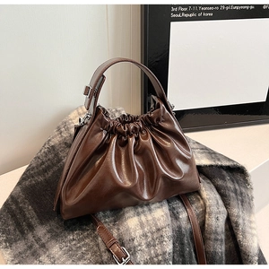 Close-up of the glossy brown pleated cloud bag on a checkered scarf with strap details