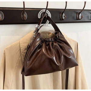 Detailed close-up of dark brown pleated cloud bag with shiny faux leather and metal hooks