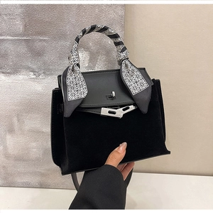 Detailed close-up of a matte black trapezoid bag with a decorative silk scarf wrap on handle
