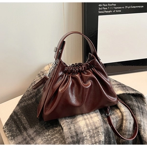 Close-up of ruched burgundy leather handbag with silver metallic buckle on textured scarf