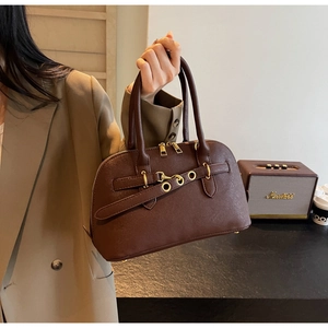 Close-up of brown textured leather shell bag with gold hardware held by a model