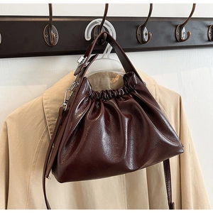 Detail view of dark brown glossy leather dumpling bag with elegant gathered pleats