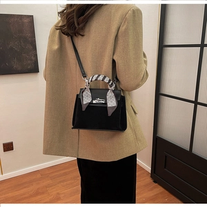 Detail of a matte black mini Kelly bag with a monochrome silk scarf handle and silver lock