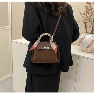 Detail of a dark brown suede handbag with a silver metal twist lock and a printed scarf