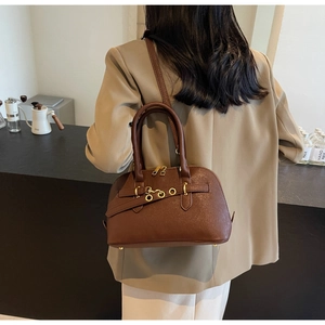 Detail of dark brown leather shell bag with gold rings shown on a model in beige suit