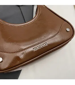 Gros plan détaillé du sac porté épaule en cuir huilé marron avec logo en métal argent
