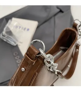 Détail du sac en cuir verni marron foncé avec chaîne argentée et anneaux métalliques