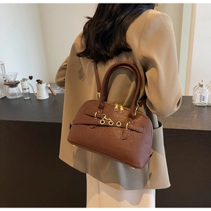 Detail shot of a dark brown crossbody bag worn by a model in a cafe setting
