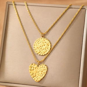 Deux colliers en acier doré avec pendentifs ronds et cœur en relief sur plateau de bijoux