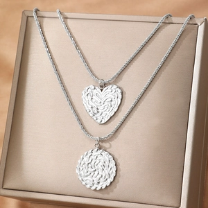 Parure collier en acier argenté avec pendentifs cœur et rond texturés sur boîte à bijoux