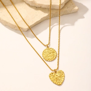 Détail d'un collier multicouche en acier doré avec pendentifs cœur et ronds texturés