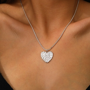 Gros plan d'un pendentif cœur argenté avec texture froissée effet lave sur une chaîne fine
