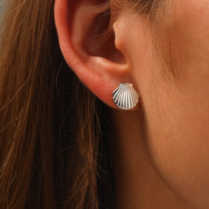 Close-up of a silver seashell stud earring on an ear, featuring elegant ribbed textures