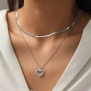 Detail of layered silver snake chain and heart pendant necklace with zircon inlay