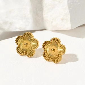 Macro shot of gold five-petal clover earrings with sunray texture and milgrain edging