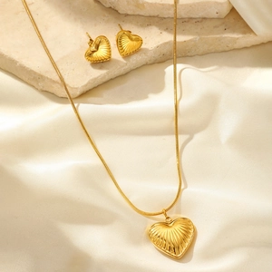Detailed shot of golden heart jewelry set with radial texture on cream silk and stone