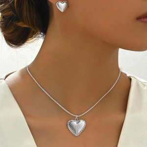 Detail of silver heart necklace and earrings set with textured radial patterns on model
