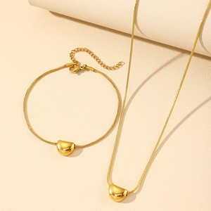 Close-up of gold bean pendants on elegant snake chains over beige leather background