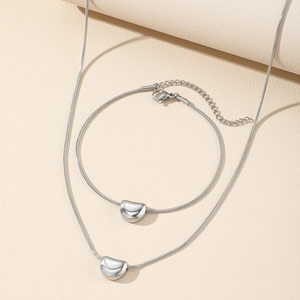Polished silver bean pendant necklace and bracelet set on beige textured leather