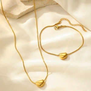 Close-up of gold bean pendant necklace and bracelet set on soft velvet background