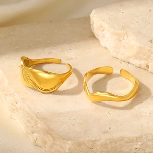 Detailed close-up of matte gold S-shaped and wide irregular open rings on stone