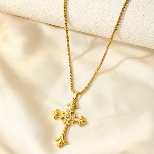 Gros plan du pendentif croix gothique dorée avec filigrane baroque et strass central