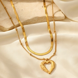 Détail de collier double rang doré avec pendentif cœur ajouré sur soie et pierre brute