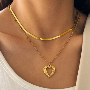 Détail du collier superposé doré avec chaîne serpent et pendentif cœur évidé et ailes