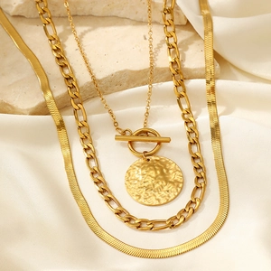 Detail of gold-layered necklace with Cuban link chain, coin pendant and toggle clasp
